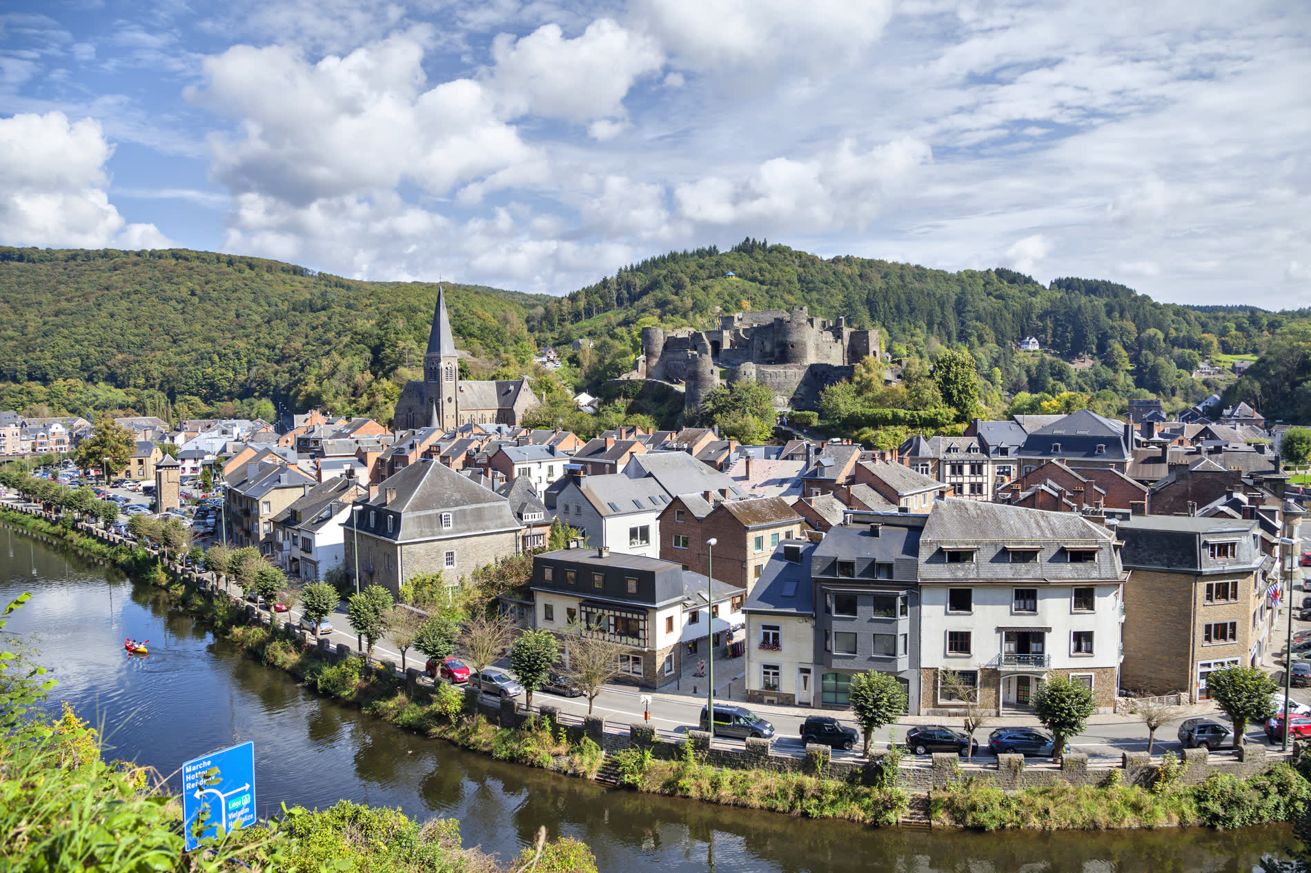 Kleinstadt an einem Fluss, darüber eine Kirche und eine Burgruine am bewaldeten Hang Kleinstadt an einem Fluss, darüber eine Kirche und eine Burgruine am bewaldeten Hang